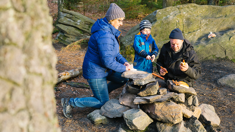 Ett par med ett litet barn grillar korv utomhus.