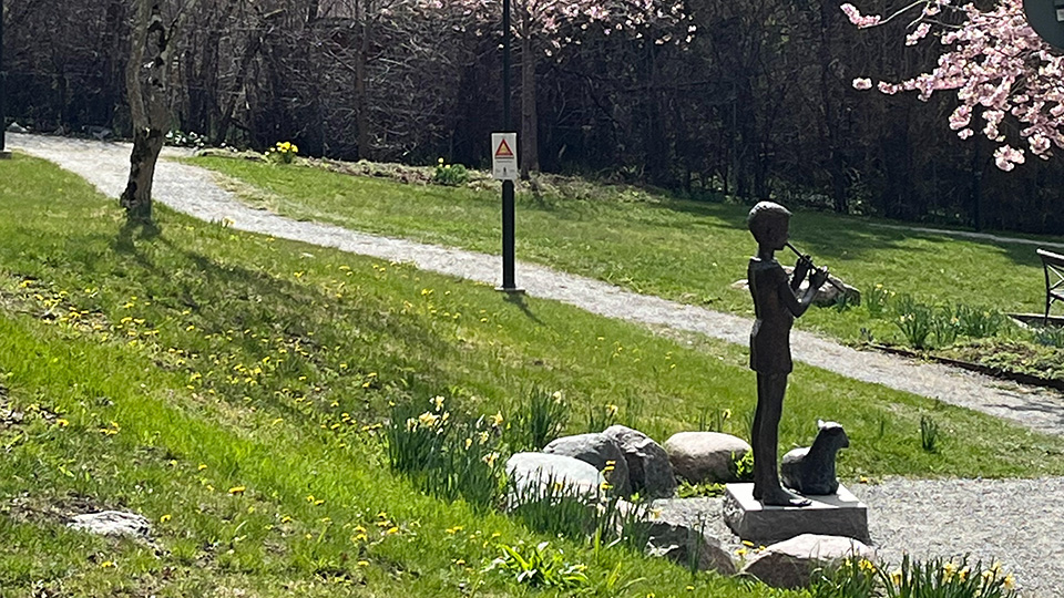 En bronsstaty av en figur som spelar flöjt. Vid hens fötter ligger ett lamm.