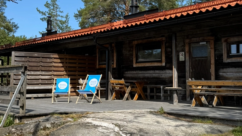 En timmerstuga med två gräsmattstolar framför.