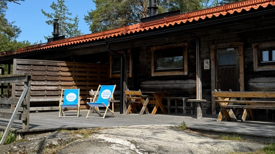 En timmerstuga med två gräsmattstolar framför.