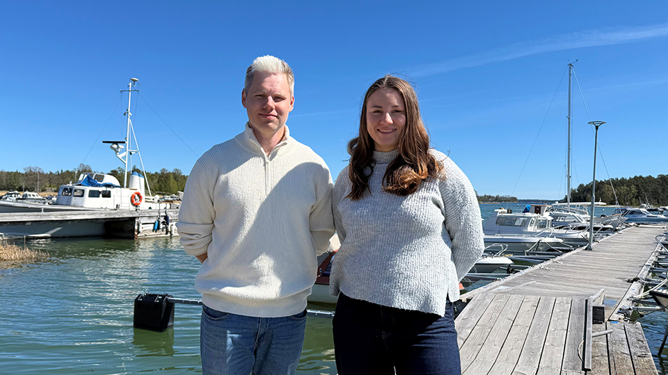 Två personer, Svante och Tove Kohala, står på en brygga med skärgårdsmiljö i bakgrunden en solig dag.