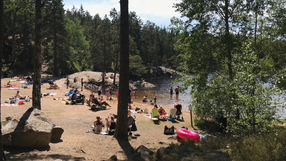 En badplats vid en sjö omgärdad av träd och klippor.