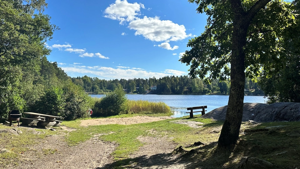 En liten badplats vid en sjö. Det finns ett bord och en bänk.