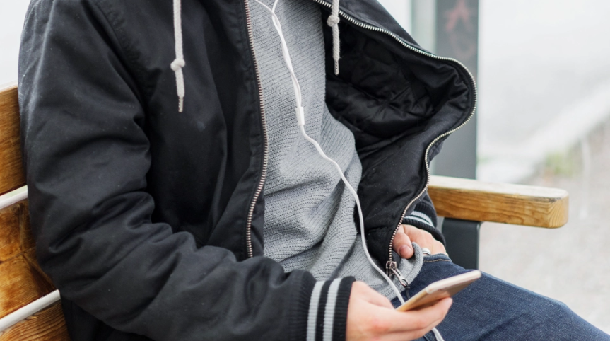 Lähikuva nuoresta joka istuu julkisessa kulkuvälineessä pidellen kännykkäänsä