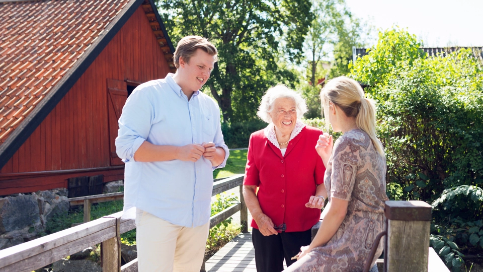 En kvinna, en yngre man och en äldre dam står ute och skrattar i solen.