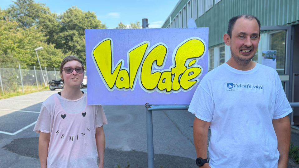Två personer står brevid en skylt där det står "valcafé".