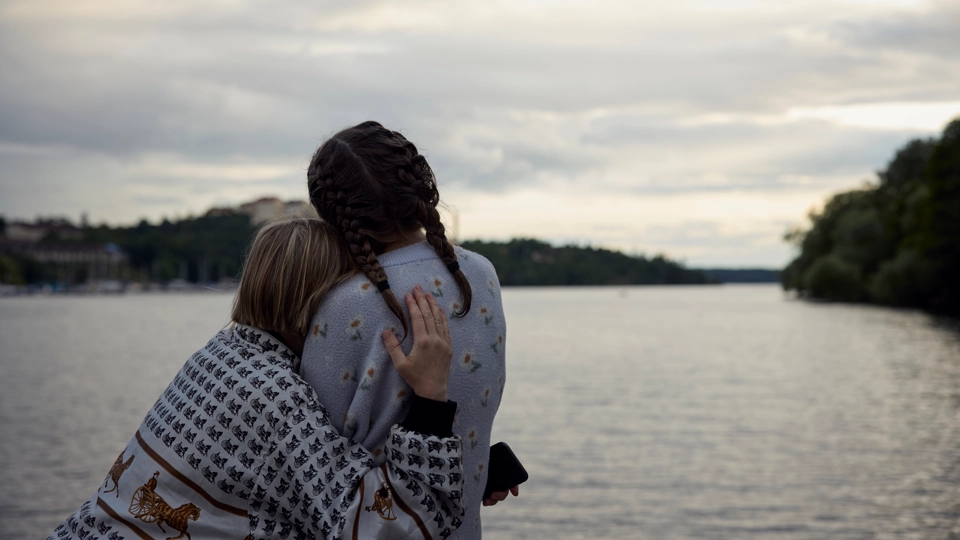 Två personer håller om varandra och tittar ut över vatten.