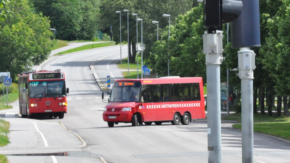 En mindre buss åker ut på en väg samtidigt som en större SL-buss åker på vägen