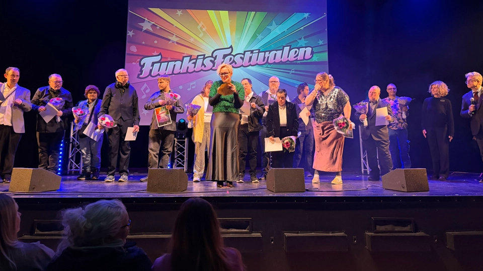 Ett gäng personer står på en scen och håller i blommor. I bakgrunden står det "Funkisfestivalen".