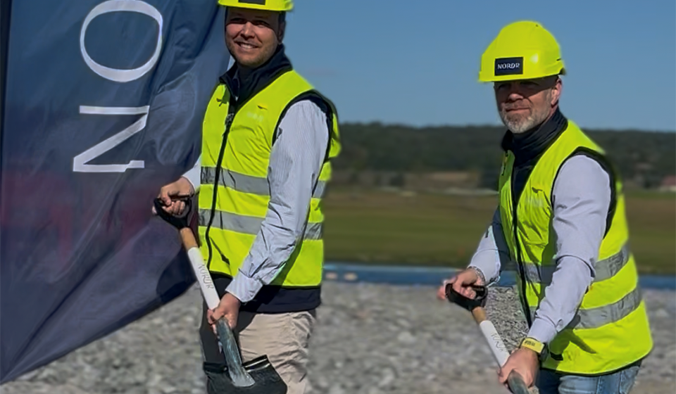 Två personer i gula varselkläder och hjälmar gräver med varsin spade.
