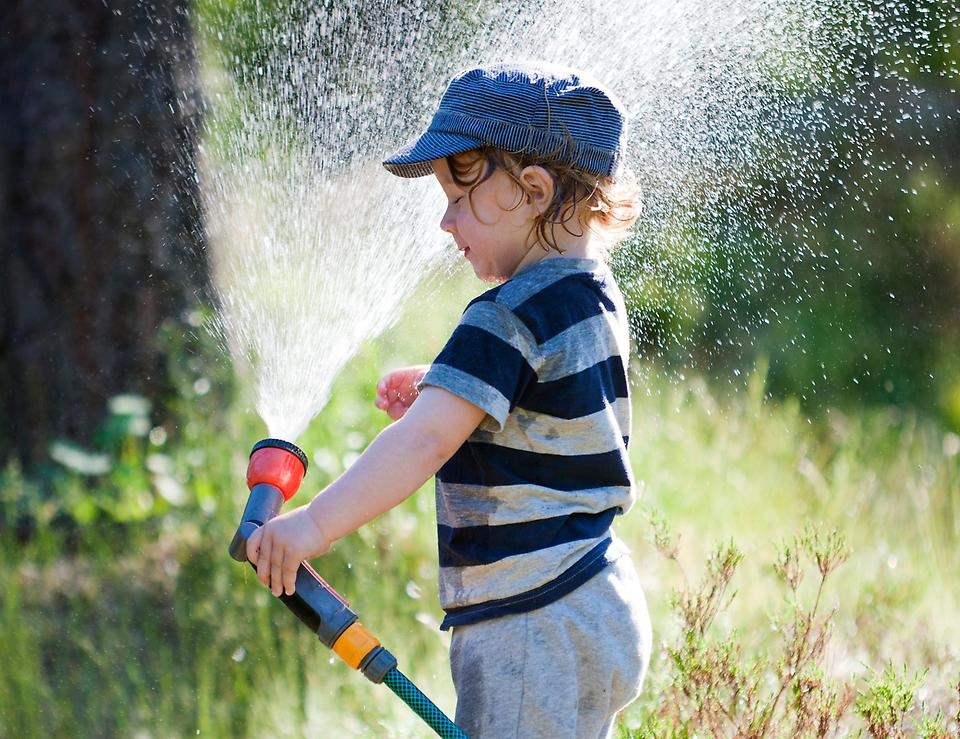 Pojke sprutar ner sig med vatten från vattenslang