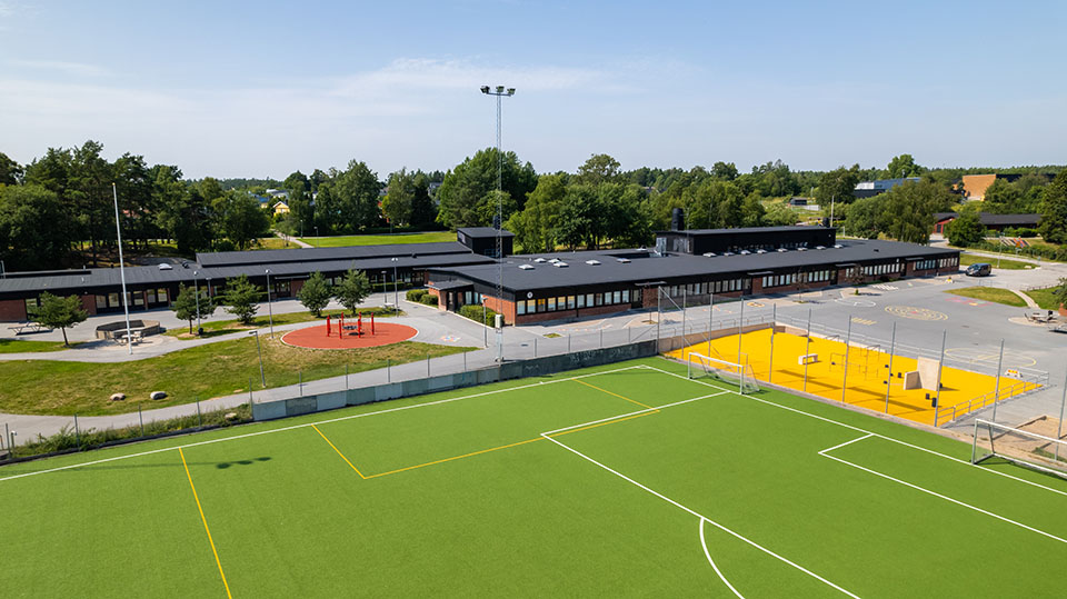 Elev som räcker upp handen i ett klassrum. Läraren går runt och hjälper till.