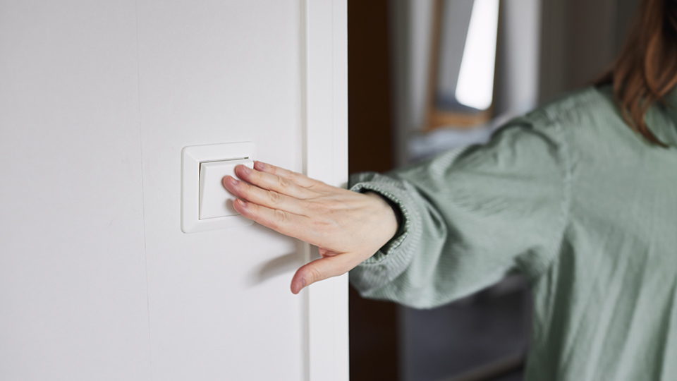 Hand som sträcker sig efter strömbrytare på väggen