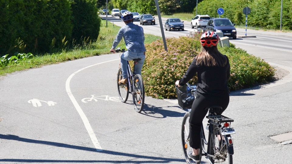 Bilden visar två cyklister bakifrån som cyklar på en gång- och cykelväg i Österåkers kommun.