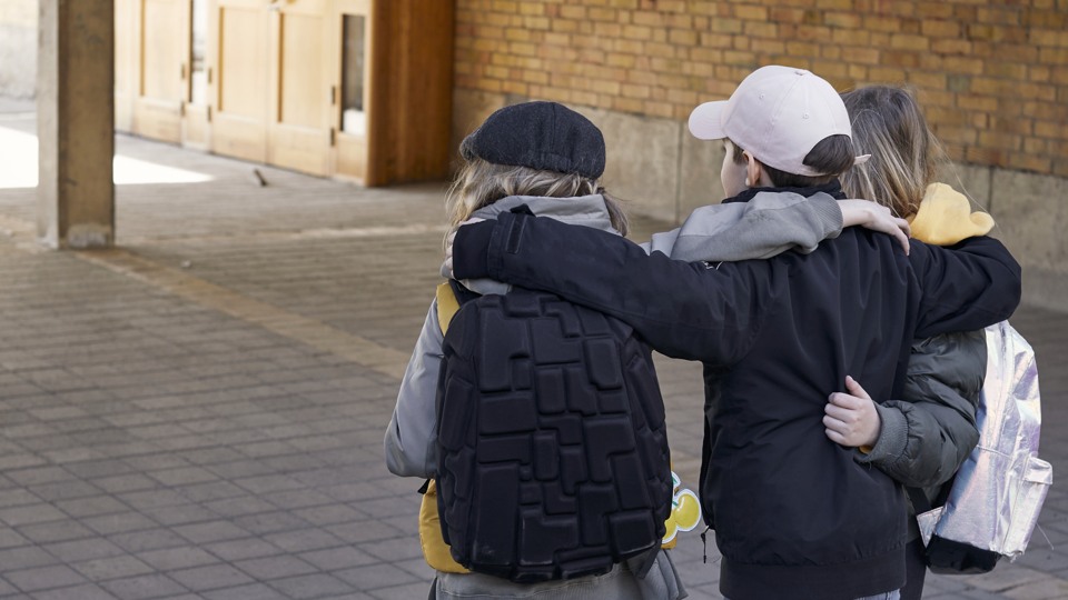 Tre elever i mellanstadieåkder står med ryggen mot kameran och håller om varandra