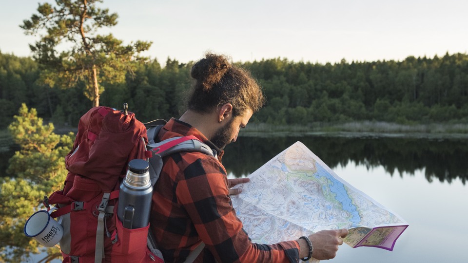 Person står vid en sjö i skogen med en karta i handen