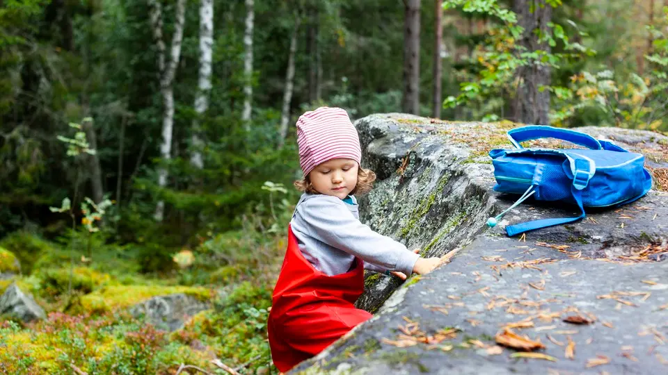 Barn leker i skogen, lutar sig mot sten