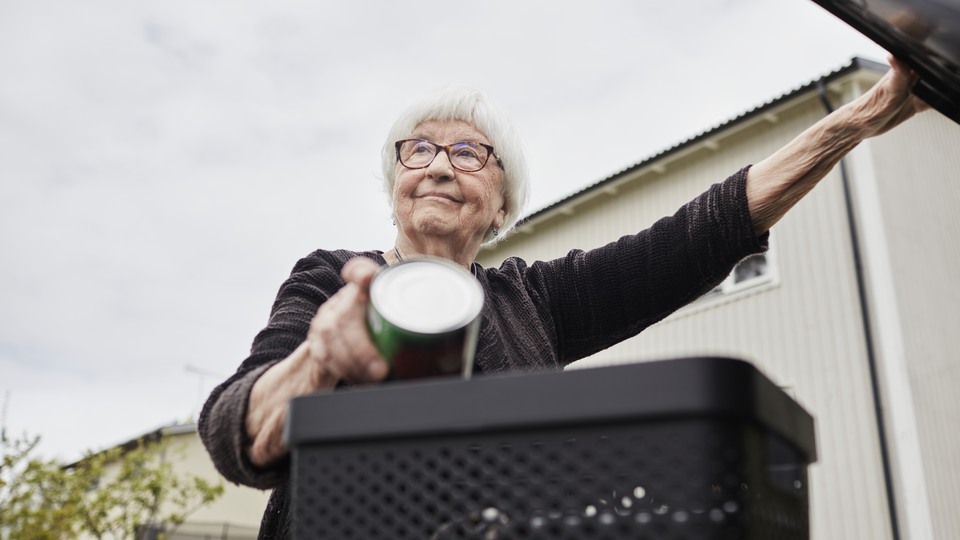 Person, senior sorterar avfall och håller upp soptunnans lock