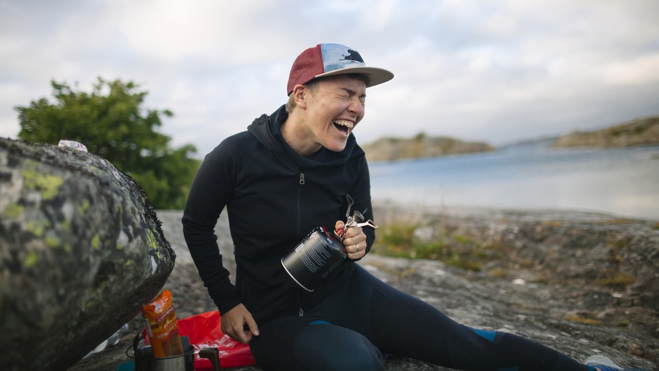 Person sitter på klippa med friluffsutrustning omkring. Skrattar