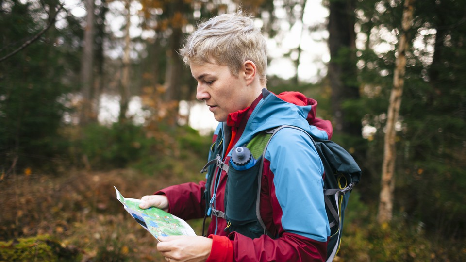 Person står i skogen, håller i en karta och bär sportkläder