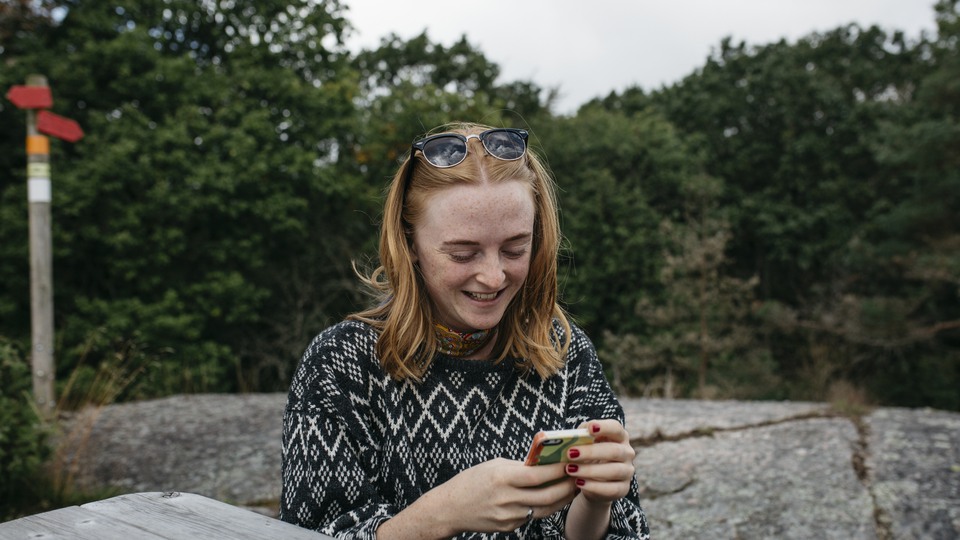 Person sitter i skärgårdsmiljö, ler och tittar ner i telefon