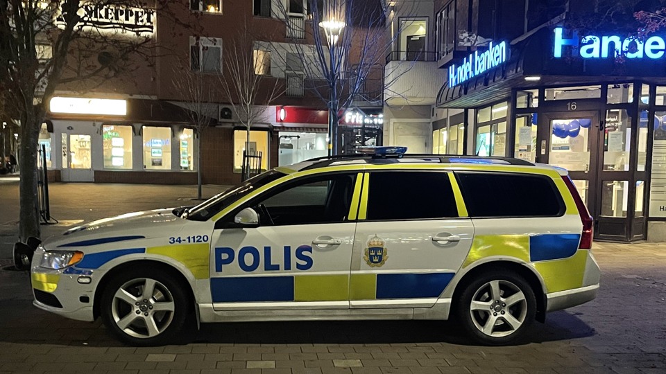 Bild på en polisbil som står på Storängstorget. Det är kväll och mörkt. Lamporna från skyltar på Åkersberga centrum lyser.