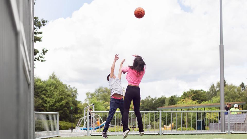 Bild på två barn som hoppar efter en basketboll som de kastat upp i luften