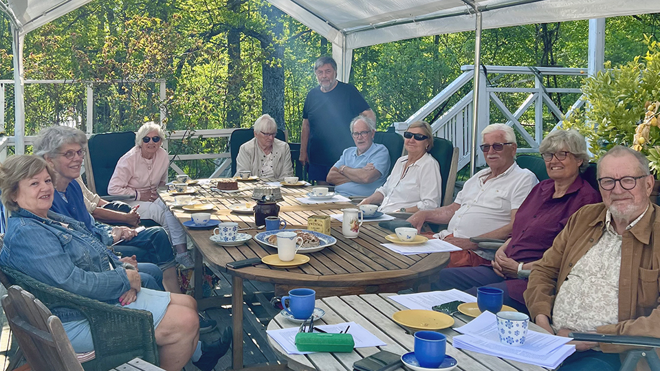 Ett dussintal personer samlade runt ett generöst kaffebord på en terrass.