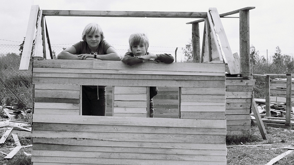 Två unga pojkar framför en trävägg som inte är färdigbyggd.