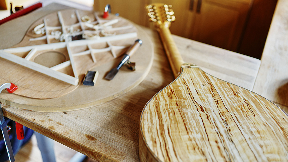 Ett stränginstrument i trä i färd att byggas. Ligger på ett bord tillsammans med diverse verktyg.