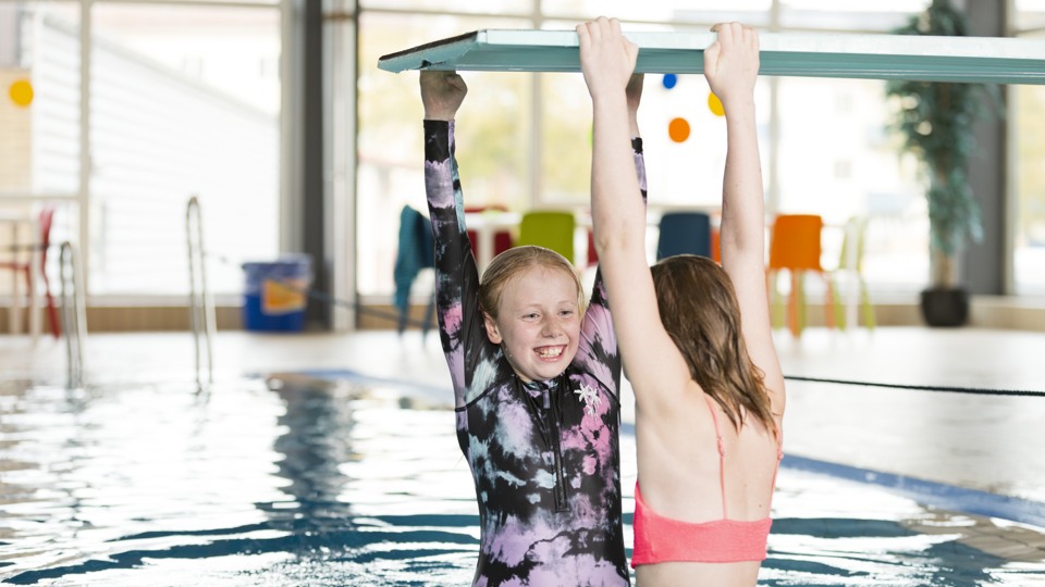 Två barn hänger i en trampolin i en simhall. De ser glada ut