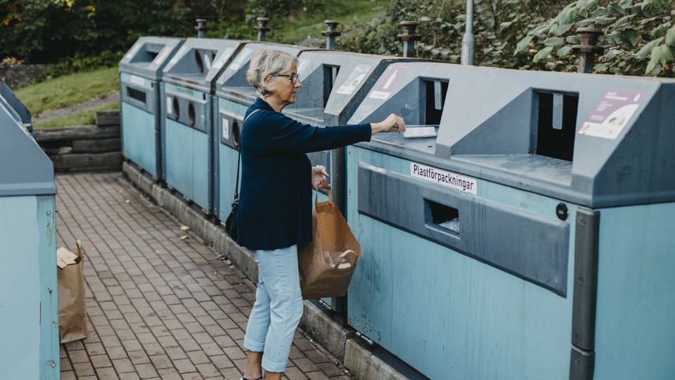 Bilden visar en kvinna som källsorterar på en miljöstation utomhus.