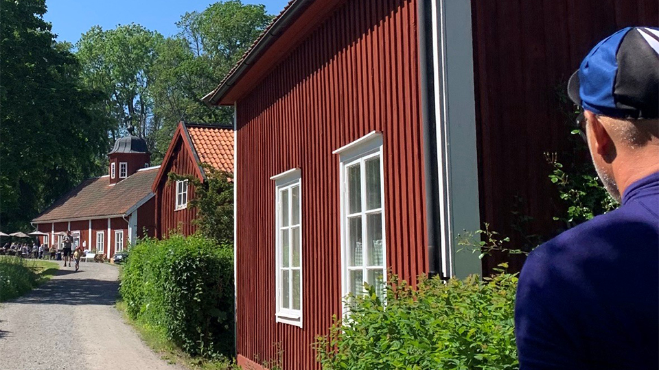 Man i sportkeps vandrar grusväg med faluröda hus och Wira Bruks kulturmiljöer.