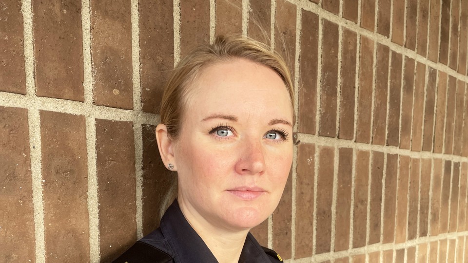 Porträttbild på trygghetssamordnare Madeleine Holmström i ljust hår mot en röd tegelvägg. 