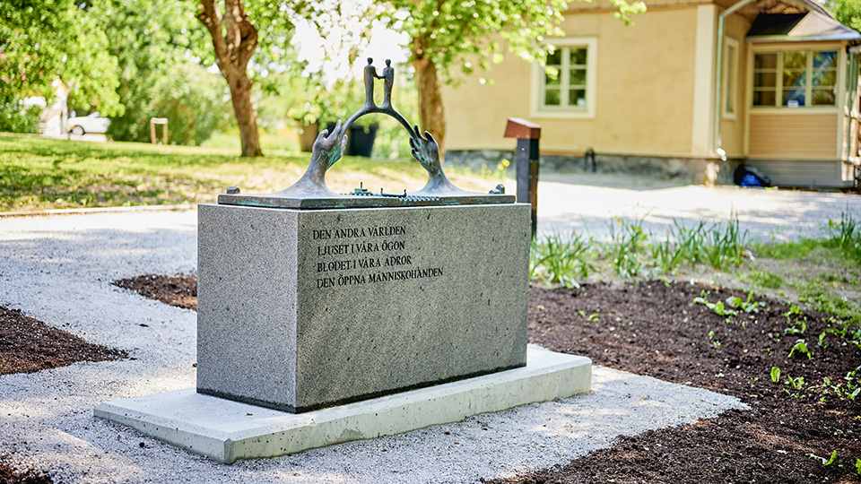 På ett betongfundament står en metallskulptur i form av två händer som möts likt en bro.