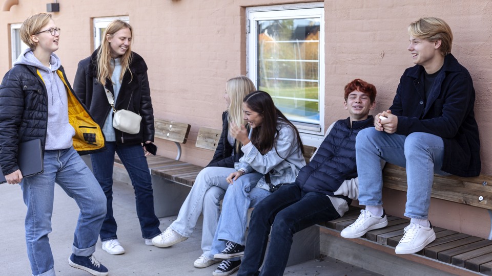 Ungdomar sitter och står utanför skolbyggnad.