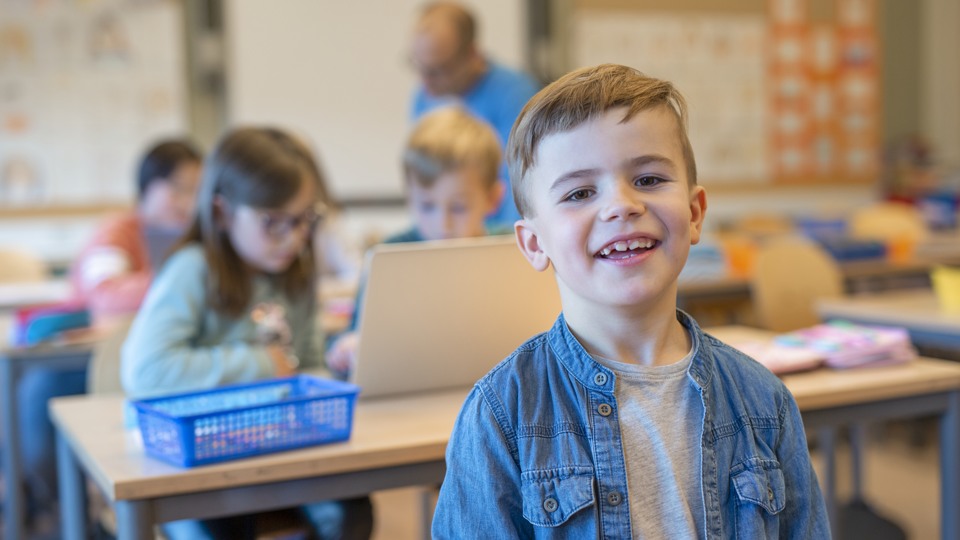 Bilden visar en glad pojke i ett klassrum