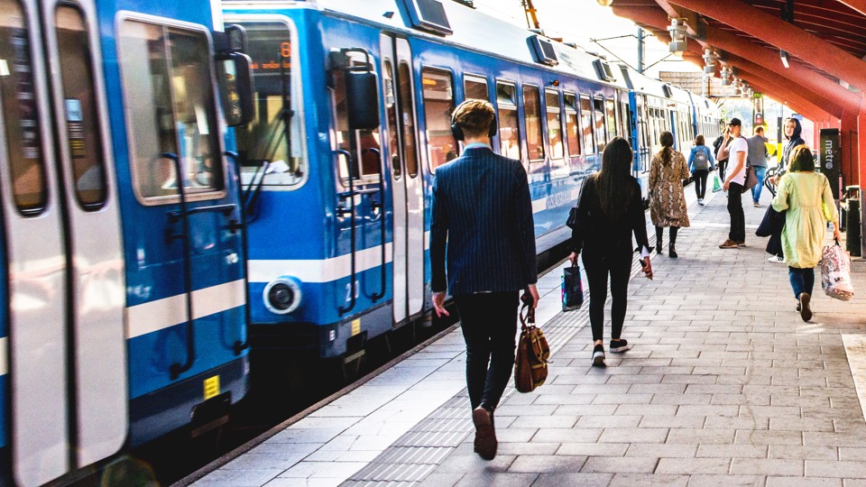 Bild på roslagsbanan som anländer på Åkersberga station. Några resenärer går på perongen.