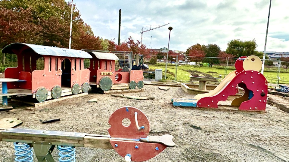 Bilden visar delar av en lekplats med ett tåg av trä i rött
