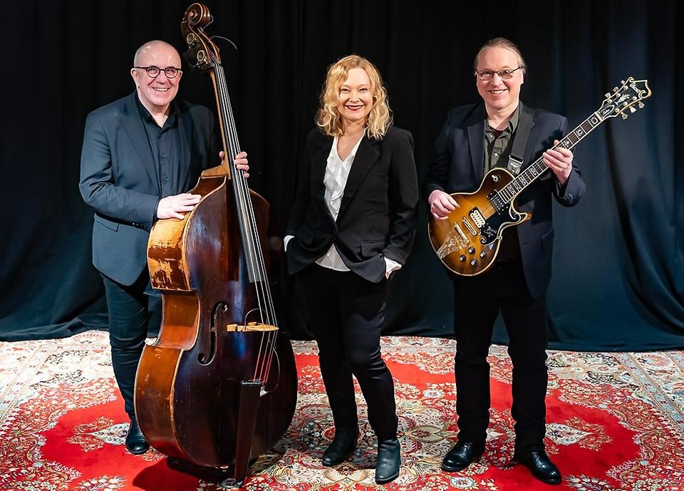 Kaksi miestä ja nainen keskellä seisoo musiikkiinstrumenttien kanssa