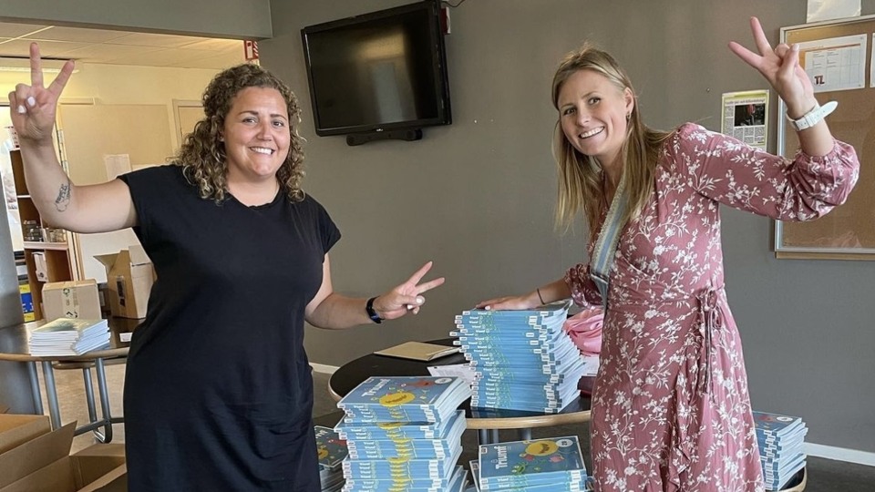 Bildem visar två glada lärare som visar upp en stor trave med läroböcker som de köpt in