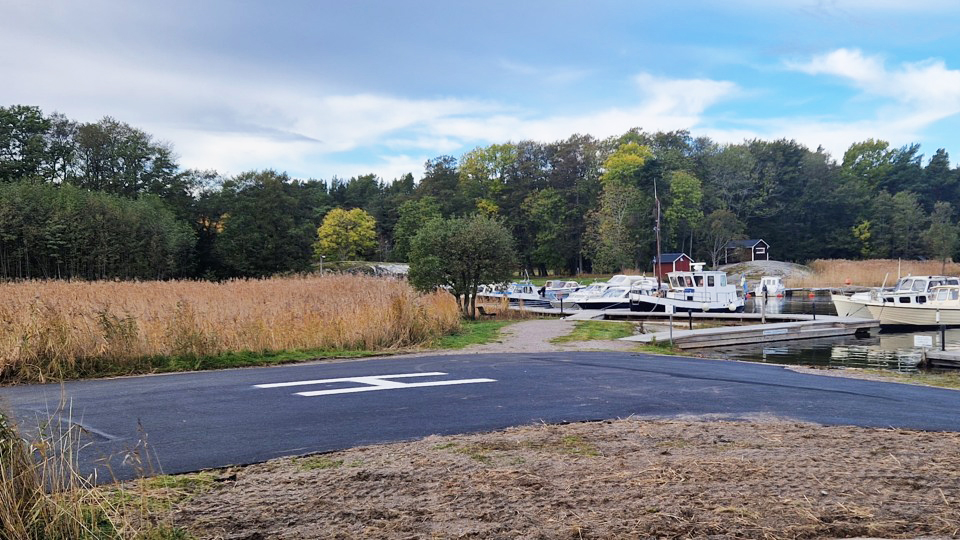 En asfalterad helikopterplatta intill en båthamn.
