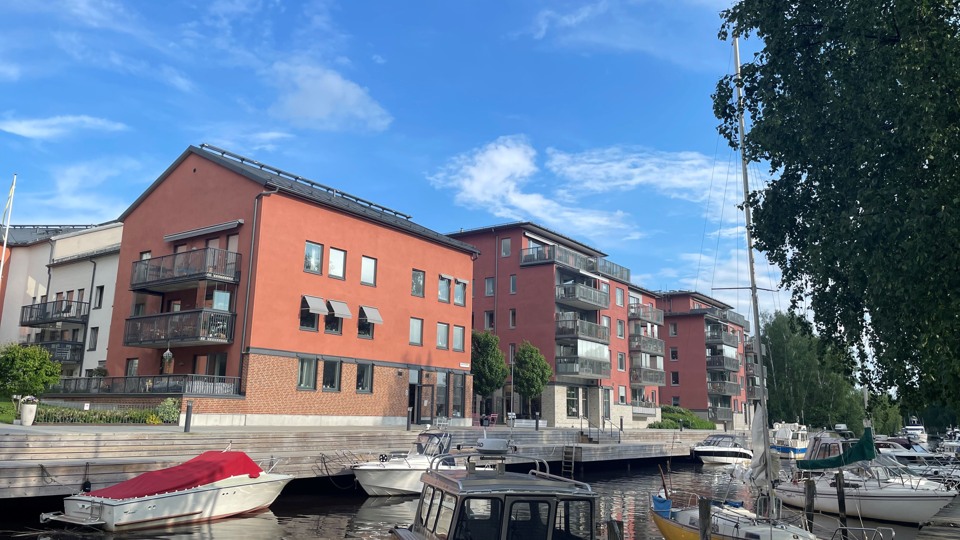 Lägenhetshus i puts i olika pastellfärger vid Åkers kanal. I kanalen ligger båtar. Himlen är blå.