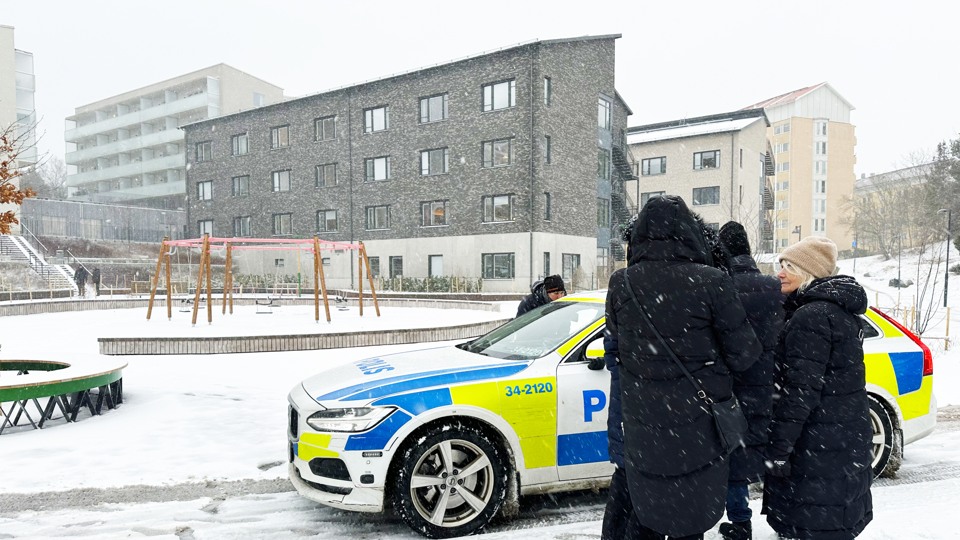 En polisbil står vid lekparken Kråkbergsparken på Norrgårdsvägen. En grupp personer som trygghetsvandrar stannar till vid polisen och utbyter några ord. Det är snö men i krukorna är påskblommor planterade.