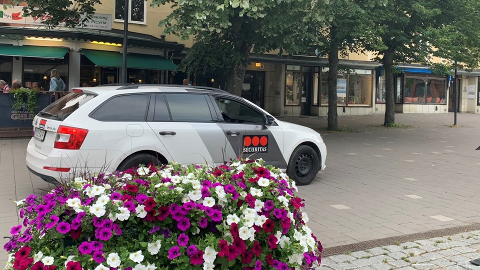 I förgrunden finns sommarblommor. Bakom syns en bil från Securitas.