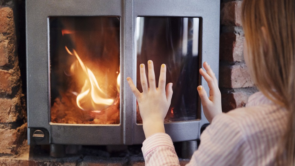 Ung flicka sitter framför en kamin där det brinner en brasa och värmer händerna