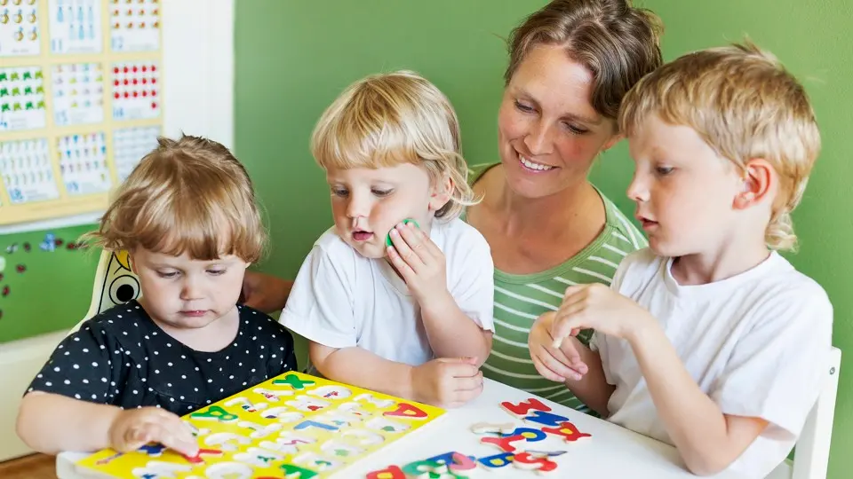 Förskolelärare och tre små ban lägger ett bokstavspussel.