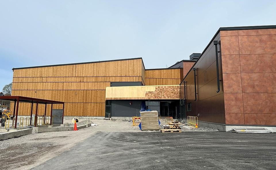 Del av fasaden på Österåkers multiarena. Den är klädd med trä och kopparfärgat material. Det syns att det fortfarande är en byggarbetsplats.