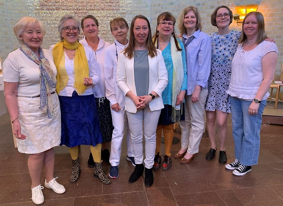Ryhmä naisia yheiskuvassa valkoisissa, sinisissä ja keltaisissa vaatteissa.