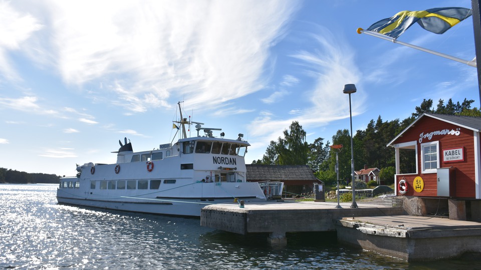Waxholmsbåt ligger vid en kaj vid skärgårdsön Ingmarsö. En svensk flagga blåser.